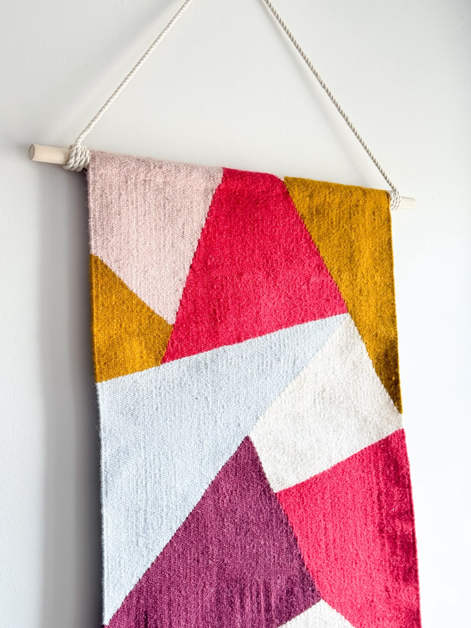 Colorful geometric patterned wall hanging on a white background