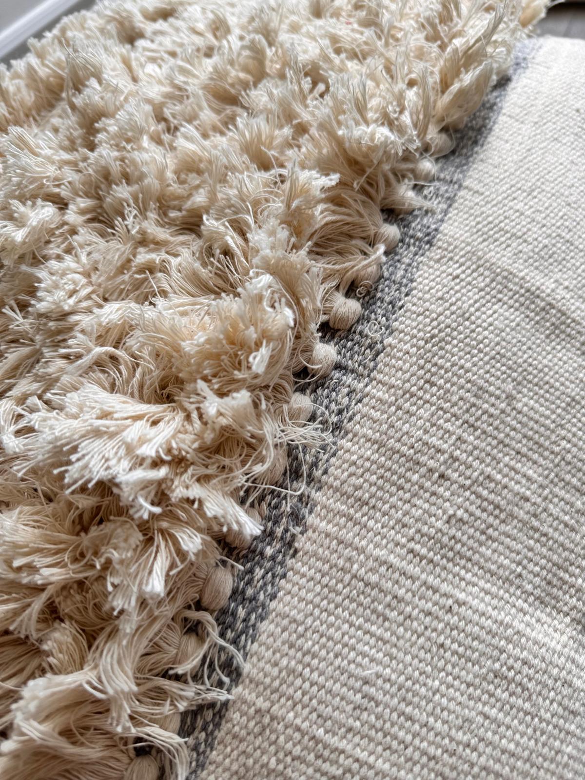 Close-up of a textured beige rug corner with a plain light gray rug.
