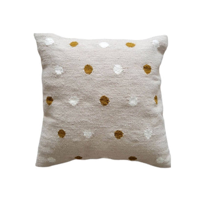 Decorative pillow with gold and white polka dot pattern on a beige background