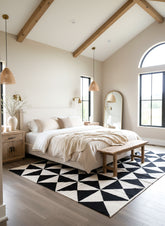 Modern bedroom with geometric rug, wooden bed frame, and pendant lights.