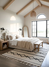 Modern bedroom with wooden beams, large window, and decorative rug.