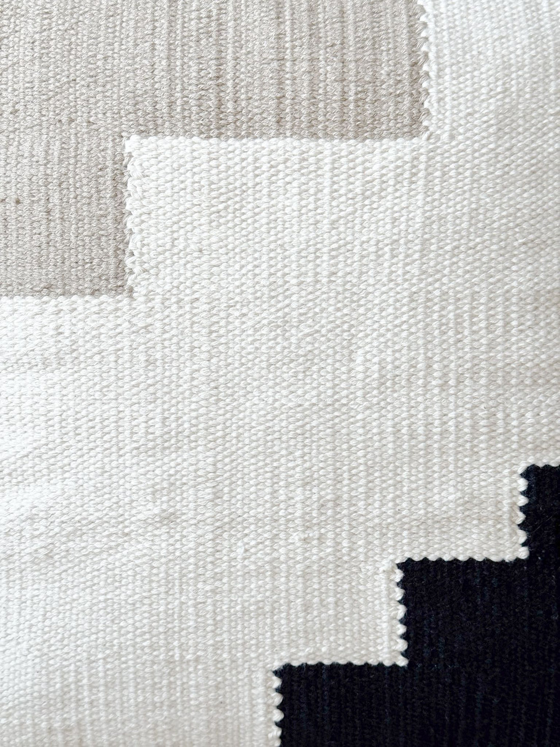 Close-up of a textured fabric with geometric pattern in beige, white, and black.